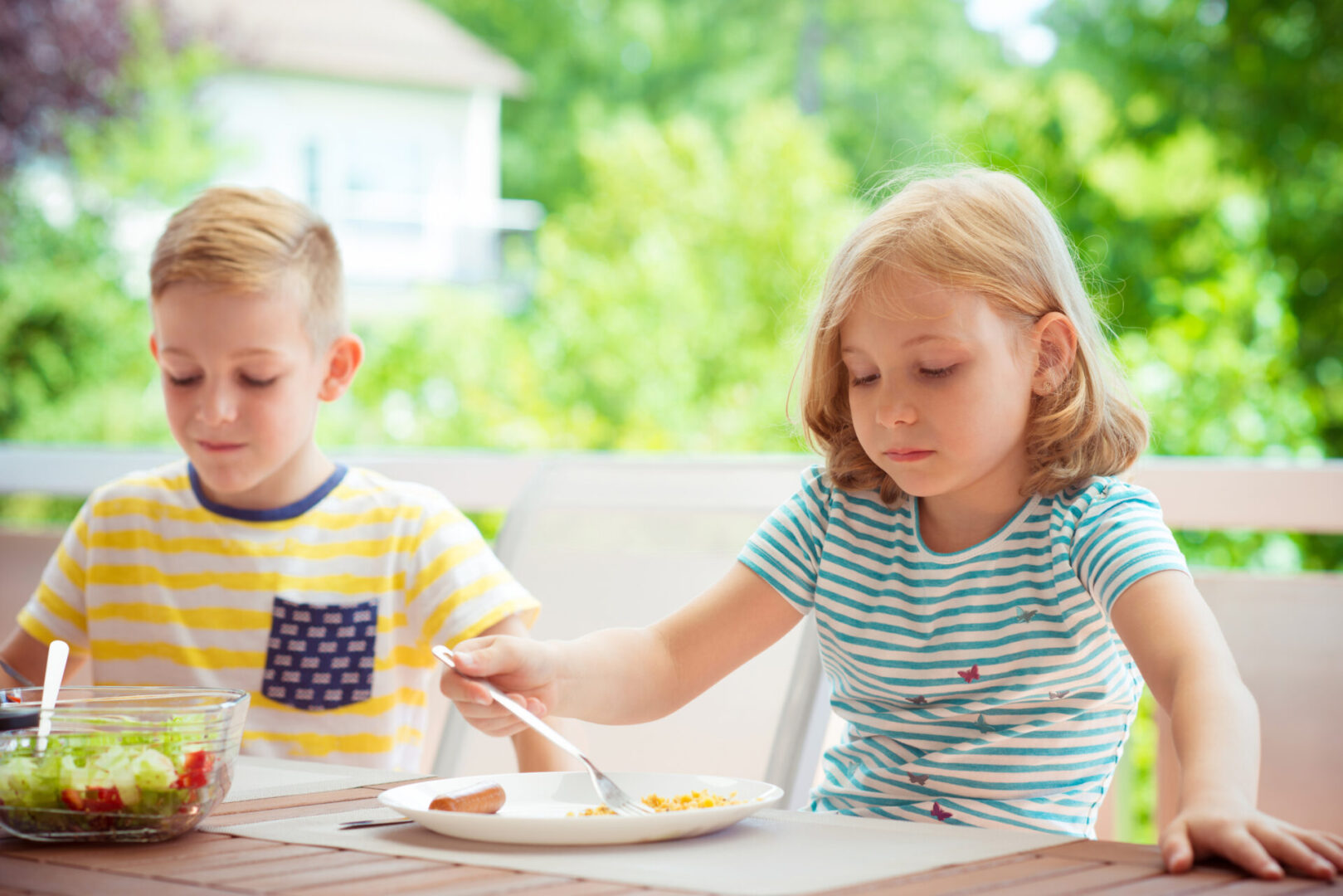 Smiling Boy Eating Food With Sister At Home Children eating at an outdoor table.