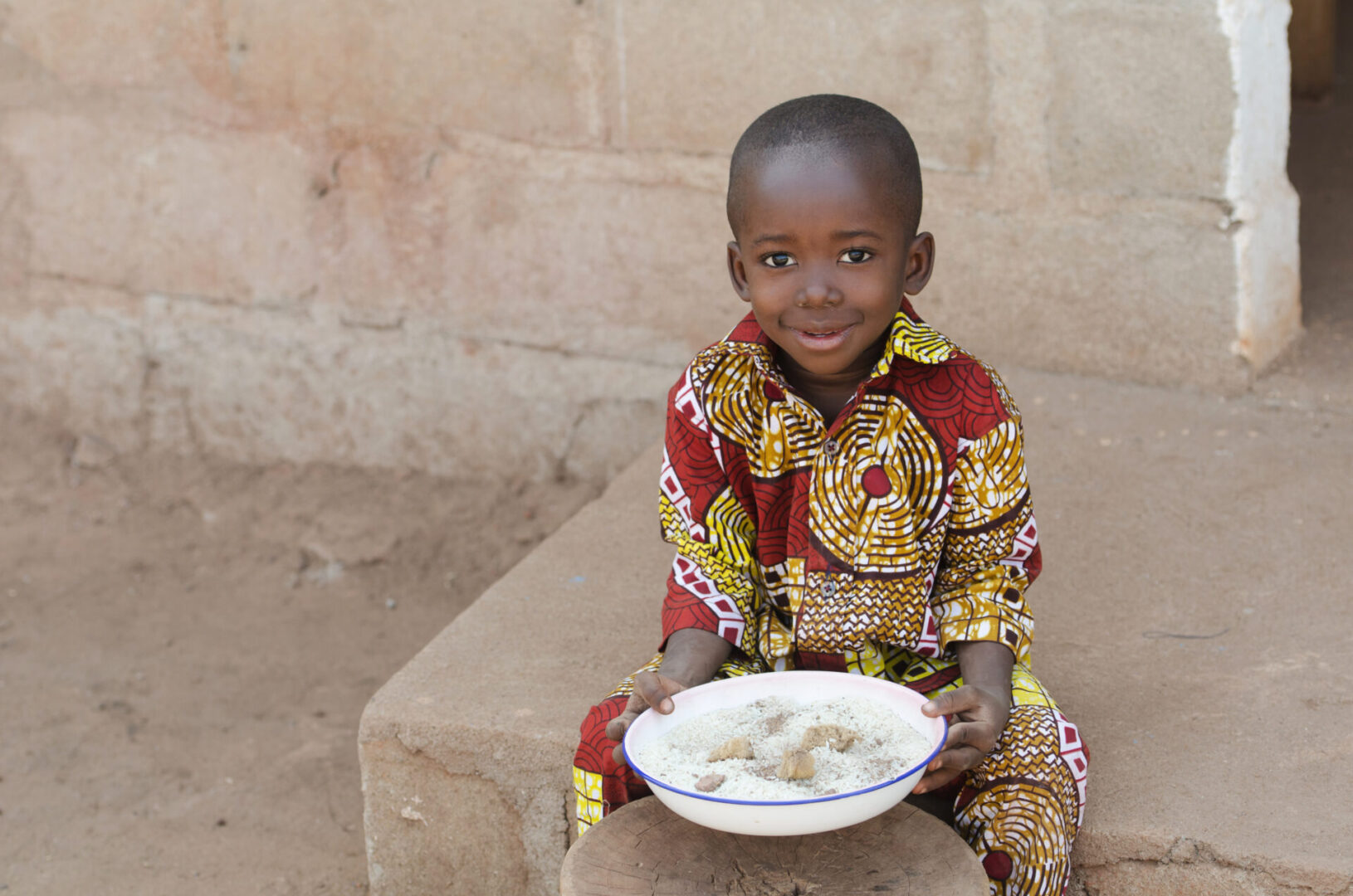 Child in colorful attire holding a bowl.