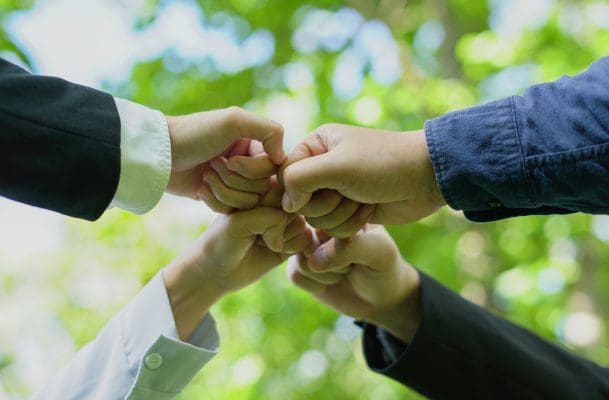 h2 (5) Hands forming a unified fist bump outdoors.