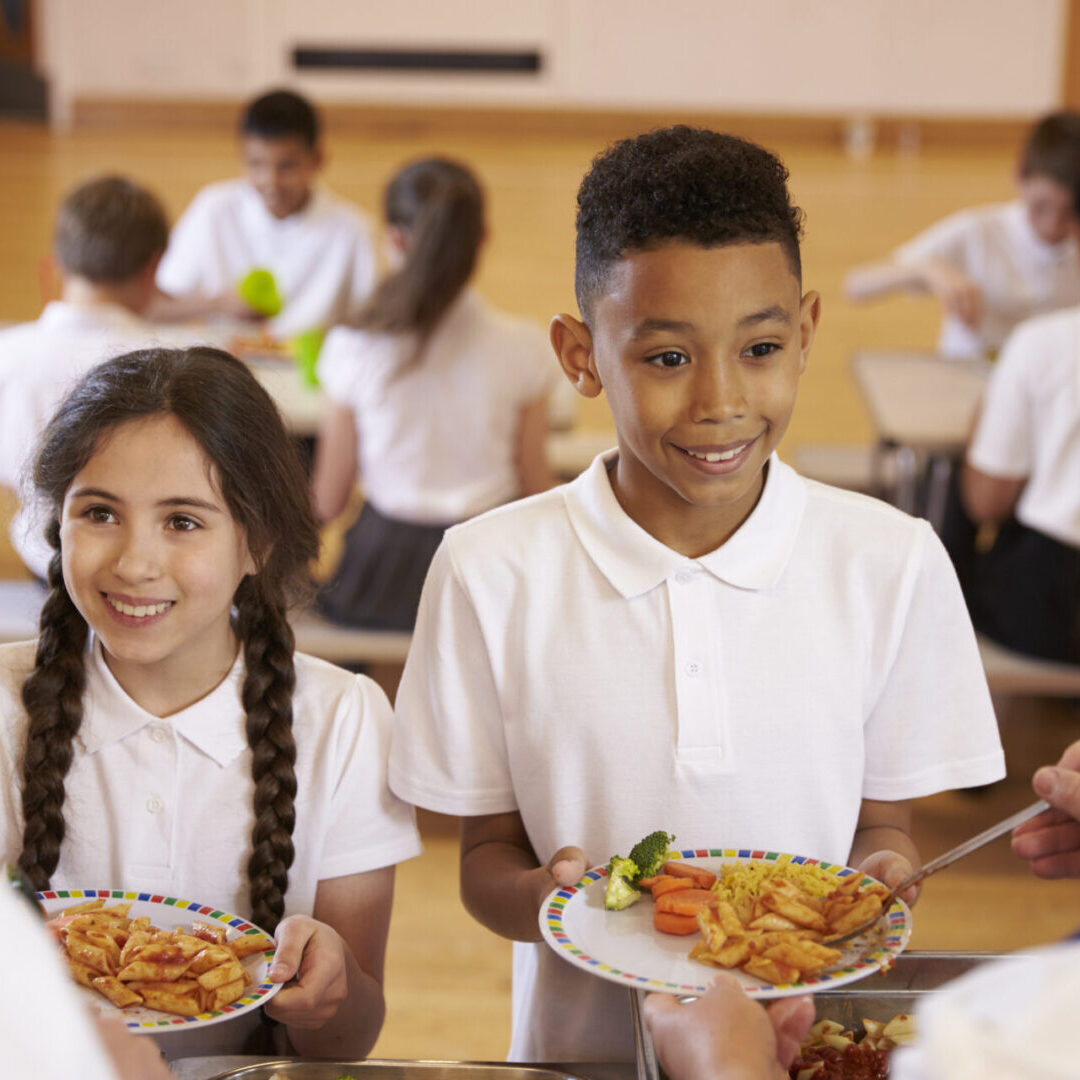 Over shoulder view of kids being served in school cafeteria Children receiving lunch in school cafeteria.